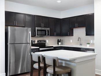 Furnished apartment kitchen with dark wood cabinets, island with bar seating and stainless steel appliances