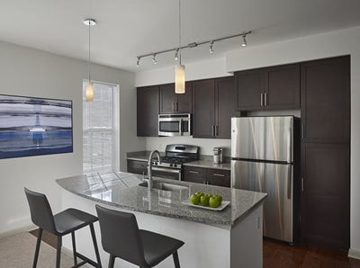 Furnished apartment kitchen with dark wood cabinets, island with bar seating and stainless steel appliances