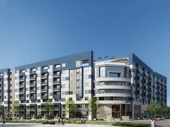 Exterior of building with large windows, cars driving by and greenery