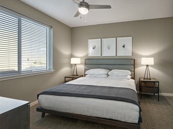 Apartment bedroom with king-sized becs, custom linen package, two night stands with lamps and overhead fan